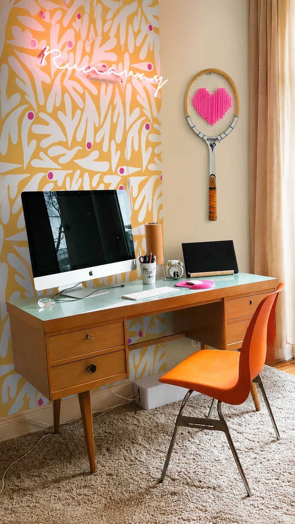 Raquette vintage au cœur rose brodé accrochée au-dessus d'un bureau vintage, sur un papier peint jaune aux motifs végétaux